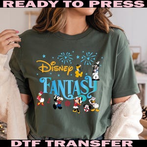 K&ouml;nnte beinhalten: Dunkelgr&uuml;nes T-Shirt mit dem Schriftzug "Disney Fantasy" in Gelb und Blau, mit Zeichentrickfiguren wie Micky Maus, Donald Duck und Goofy. Das Design umfasst Feuerwerk und Sterne.