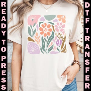 May include: Cream-colored t-shirt featuring a colorful floral design in a square arrangement. The design includes flowers in shades of peach, pink, and purple, with green leaves and accents. The words "READY TO PRESS" and "DTF TRANSFER" are printed vertically on the sides.