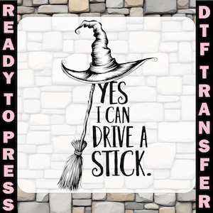 May include: Black and white graphic of a witch's hat and broomstick with the text "YES I CAN DRIVE A STICK." The image is a ready-to-press DTF transfer, perfect for creating custom apparel and accessories.