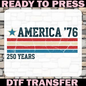 May include: A DTF transfer featuring the text "AMERICA '76" with a blue star and red, cream, and blue stripes. The words "250 YEARS" are below the stripes. The words "READY TO PRESS" and "DTF TRANSFER" are at the top and bottom.