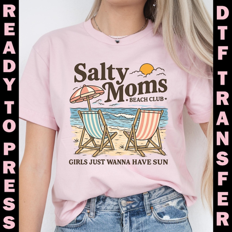 May include: A light pink t-shirt featuring a beach scene with two striped beach chairs, an umbrella, and the text "Salty Moms Beach Club." The phrase "Girls Just Wanna Have Sun" is also printed on the shirt.