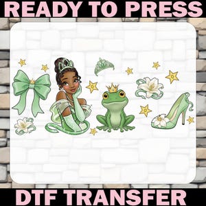 May include: A DTF transfer design featuring a princess, a frog with a crown, a high-heeled shoe, a bow, and stars. The design is in shades of green, white, and gold, with the text "READY TO PRESS" and "DTF TRANSFER".