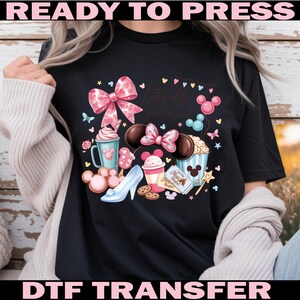 Puede incluir: Camiseta negra con un gr&aacute;fico colorido que presenta un lazo rosa, orejas de Mickey Mouse y varias golosinas tem&aacute;ticas de Disney. Tambi&eacute;n se incluye el texto "Literally just a girl". Las palabras "READY TO PRESS" y "DTF TRANSFER" est&aacute;n arriba y abajo.