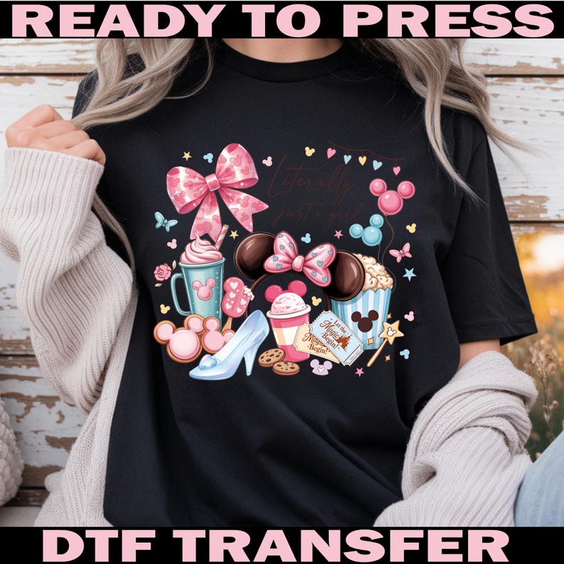 Puede incluir: Camiseta negra con un gr&aacute;fico colorido que presenta un lazo rosa, orejas de Mickey Mouse y varias golosinas tem&aacute;ticas de Disney. Tambi&eacute;n se incluye el texto "Literally just a girl". Las palabras "READY TO PRESS" y "DTF TRANSFER" est&aacute;n arriba y abajo.
