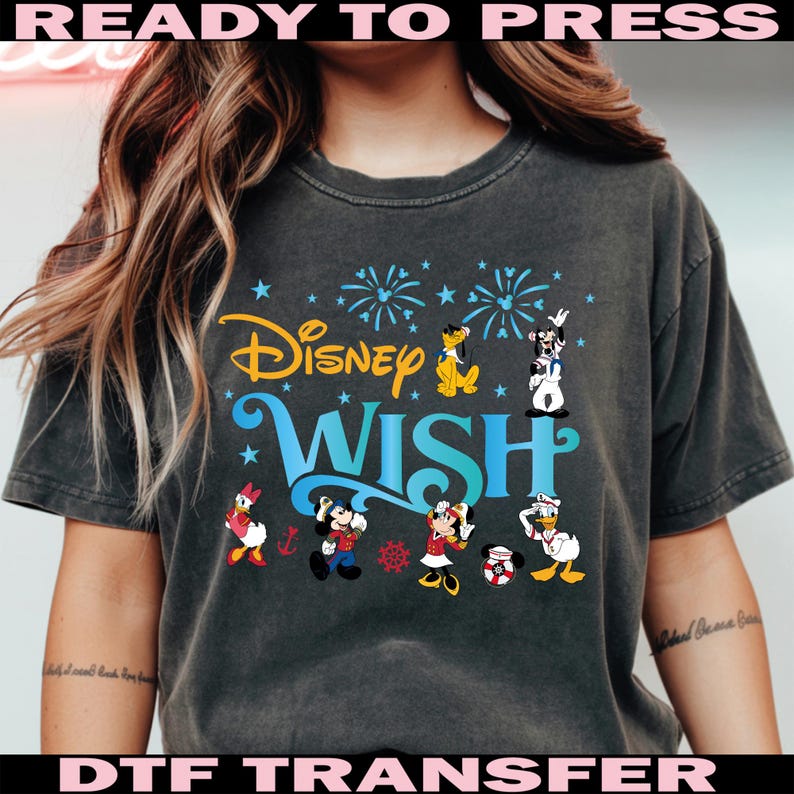 K&ouml;nnte beinhalten: Dunkelgraues T-Shirt mit den Worten "Disney Wish" in Gelb und Blau sowie Disney-Figuren. Das Shirt tr&auml;gt auch die Worte "READY TO PRESS" und "DTF TRANSFER" in Pink.