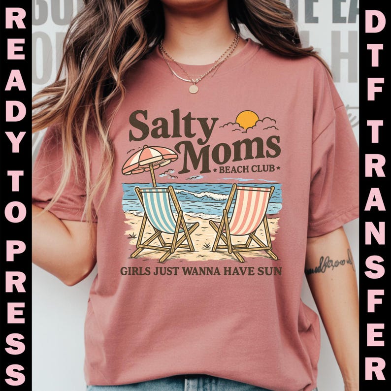 May include: A dusty rose t-shirt featuring a beach scene with two beach chairs, an umbrella, and the text "Salty Moms Beach Club." The phrase "Girls Just Wanna Have Sun" is also printed on the shirt. The words "Ready to Press" and "DTF Transfer" are printed on the sides.
