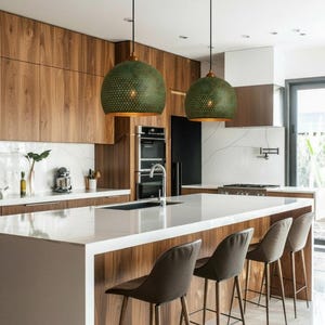 May include: Modern kitchen with a white countertop island and wooden cabinetry. Two green pendant lights hang above the island. Brown bar stools are lined up along the island. The kitchen features stainless steel appliances and a marble backsplash.