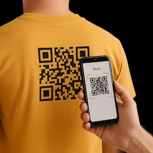 May include: Mustard yellow t-shirt featuring a large black QR code on the back. A smartphone displays a similar QR code with the word "Scan" on the screen. The phone is held up to the shirt.
