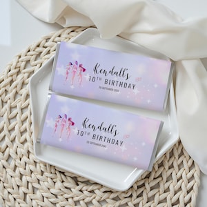 Könnte beinhalten: Zwei Schokoriegelverpackungen mit einem Lavendel- und rosafarbenen Farbverlauf. Die Verpackungen zeigen den Text "Kendalls 10. Geburtstag" und eine Grafik von drei Figuren. Weiße Sterne und Herzen sind ebenfalls vorhanden.