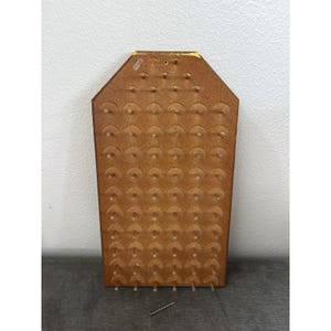 May include: A brown, coffin-shaped wooden pegboard featuring a grid of evenly spaced holes and small wooden pegs. The board has a flat top edge with a yellow accent and a tapered base. A single metal screw is positioned below the board.