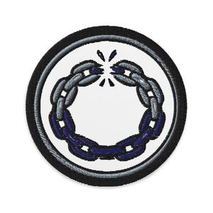 May include: Embroidered patch featuring a broken chain design. The patch has a white center with a blue and gray chain design, encircled by a gray and black border. The chain is broken at the top, symbolizing freedom or liberation.