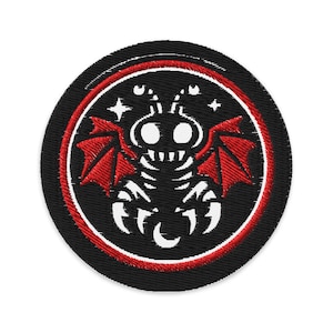 May include: Embroidered patch featuring a stylized black creature with red bat-like wings, white teeth, and two large eyes. The design is set within a black circle with a red and white border, and includes stars and crescent moons.
