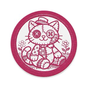 Może przedstawiać: Okrągła, magenta naszywka z wyszywanym wzorem kota. Kot ma guziczkowe oczy i kapelusz, z patchworkowym wzorem. Dwa kwiaty flankują kota na białym tle, otoczone magentową obwódką.