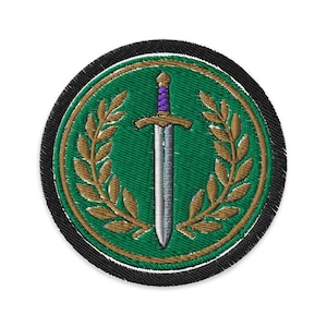 May include: Embroidered patch with a green background, featuring a silver sword with a purple handle. The sword is centered within a gold laurel wreath. The patch has a black border and a gold outline.