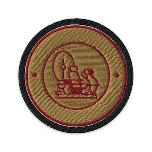 Pode incluir: Patch bordado com um design circular. O patch apresenta um fundo bege com um design vermelho e bege no centro. A borda externa é preta. O design parece ser uma ilustração estilizada.