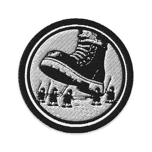 May include: Embroidered patch featuring a large black boot stepping on small figures. The design is set within a white circle, framed by a black border. The patch is round and has a textured appearance.