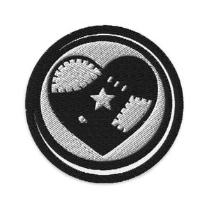 Może przedstawiać: Haftowana naszywka z czarnym wzorem serca i białym obramowaniem. Serce zawiera gwiazdę i inne kształty. Naszywka jest okrągła z czarnym obramowaniem zewnętrznym i białym wewnętrznym.