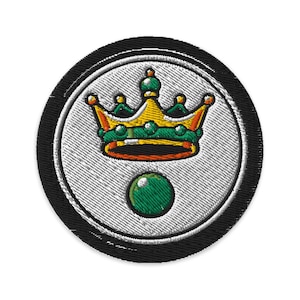 Könnte beinhalten: Gestickter Aufnäher mit einem gold-grünen Kronen-Design auf einem weißen Kreis, darunter eine grüne Kugel. Der Aufnäher hat einen schwarzen Rand, geeignet für Kleidung oder Accessoires.