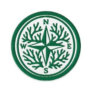 May include: Embroidered patch featuring a compass rose design. The patch has a white background with a green border and a green compass rose in the center. The cardinal directions are labeled with white letters.