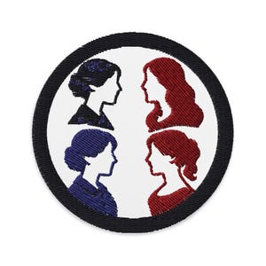 Op de afbeelding: Geborduurde patch met vier vrouwenprofielen in een cirkel. De profielen zijn in zwart, rood en blauw, tegen een witte achtergrond, met een zwarte rand. Het ontwerp is een eenvoudige, maar elegante weergave.