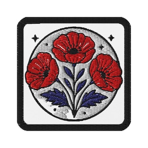 Könnte beinhalten: Gestickter Aufnäher mit drei roten Mohnblumen mit schwarzen Zentren, blauen Blättern und Stielen. Das Design befindet sich auf einem weißen Hintergrund in einem kreisförmigen Rahmen, umgeben von einem schwarzen quadratischen Rand. Kleine Sternakzente.