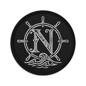 May include: Embroidered patch with a nautical theme. The design features a white ship's wheel, the letter "N", and stylized waves, all on a black circular background. The patch is likely for clothing or accessories.