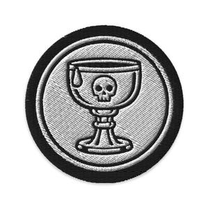 May include: Embroidered patch featuring a chalice with a skull inside, a drop of liquid, and a detailed base. The design is in shades of gray and white, set against a black circular border. The patch has a textured appearance.