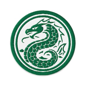以下が含まれることがあります： 白い背景に緑色の蛇のデザインが施された、円形の刺繍パッチ。緑色の縁で囲まれています。蛇は鱗と湾曲した形で描かれています。パッチは布製です。