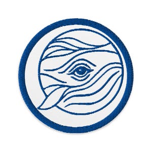 May include: Embroidered patch featuring a blue and white whale design. The whale is depicted with stylized lines and a single eye, set within a white circle and a blue border. The patch is round.