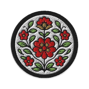 May include: Embroidered circular patch featuring a floral design. The patch has a black border, a white background, and a central arrangement of red flowers with green leaves. The flowers have yellow centers.