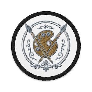 Op de afbeelding: Geborduurde patch met een schilderspalet en twee gekruiste penselen. Het palet is bruin met verfputten. Het ontwerp is omcirkeld door een zilveren decoratieve rand en een zwarte buitenrand. Een creatief kunstthema.