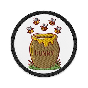 May include: Embroidered patch featuring a brown honey pot with the word "HUNNY" and dripping honey. Six cartoon bees fly above the pot. The patch has a white background and a black border.