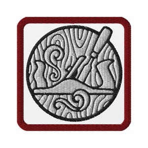 May include: Embroidered patch with a woodworking theme. The patch has a white background with a circular design of a hand plane and wood grain, outlined in black. The patch is bordered by a dark red edge.