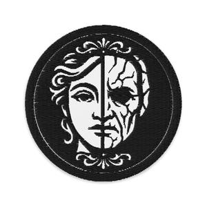 Può includere: Una toppa rotonda nera con un design a volto diviso. Una metà raffigura un volto giovane, l'altra un volto invecchiato, entrambi in bianco. La toppa ha un bordo bianco e decorazioni.