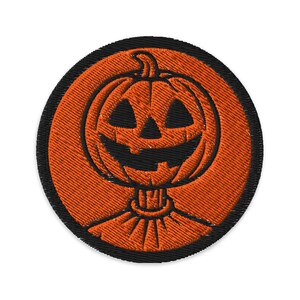 May include: Embroidered patch featuring a smiling jack-o'-lantern design. The pumpkin is orange with black facial features and stem, set against an orange background with a black border. Perfect for Halloween.