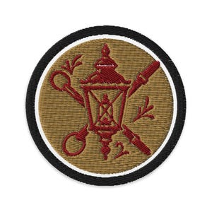 Könnte beinhalten: Gestickter Aufnäher mit kreisförmigem Design. Der Aufnäher hat einen beigefarbenen Hintergrund mit einer roten Laterne, gekreuzten Schlüsseln und einer Feder. Das Design wird von einem weißen und schwarzen Ring umrandet.