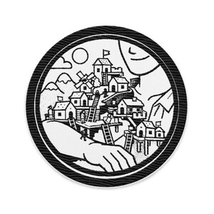 May include: Circular black and white patch featuring a detailed illustration of a village nestled in a mountain landscape. The design includes houses, ladders, and a hand, all within a textured border.