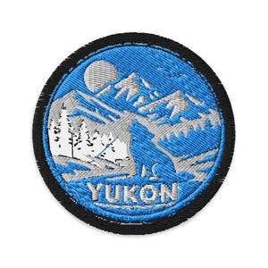 May include: Embroidered patch featuring a blue howling wolf in a mountain landscape with a full moon. The word "YUKON" is embroidered in white at the bottom. The patch has a black border and is circular in shape.