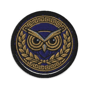 May include: Embroidered patch featuring a stylized owl design. The owl is centered on a dark blue background, surrounded by a gold laurel wreath and a Greek key border. The patch has a black border.