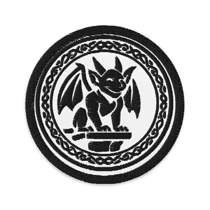 Könnte beinhalten: Gestickter Aufnäher mit einem schwarzen Gargoyle-Design auf weißem Hintergrund, umrahmt von einem dekorativen Rand. Der Aufnäher hat einen schwarzen Außenrand. Der Gargoyle hat Flügel und sitzt auf einem Steinsockel.