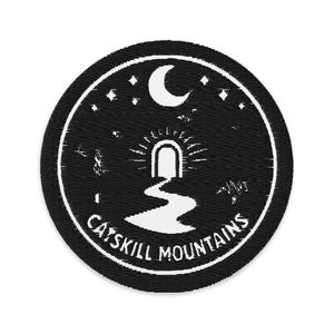 May include: Round black patch with a white embroidered design featuring a crescent moon, stars, and a path leading to a glowing archway. The text "CATSKILL MOUNTAINS" is in a white, curved font around the bottom edge.