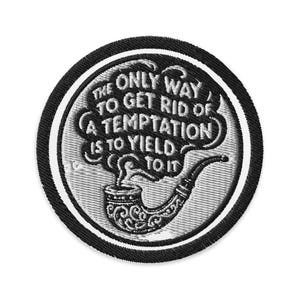 May include: A round, black and white embroidered patch with the quote, "The only way to get rid of a temptation is to yield to it." The design includes a smoking pipe with decorative scrollwork and a smoke cloud.