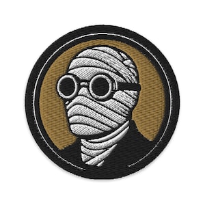 May include: Embroidered patch featuring a stylized image of a figure with bandages covering the face and wearing round glasses. The design is set against a gold background within a black circular border.