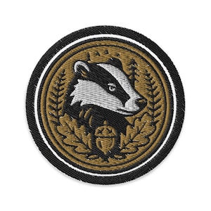 May include: Embroidered patch featuring a badger in a circular design. The badger is black and white, surrounded by a gold-colored oak leaf and acorn design. The patch has a black border with a white inner border.
