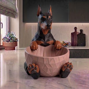 Peut inclure: Une sculpture géométrique de Doberman Pinscher noir et marron, tenant un bol rose clair. Les pattes et le visage du chien sont détaillés. Le bol a un motif géométrique. La sculpture est sur une surface en marbre.