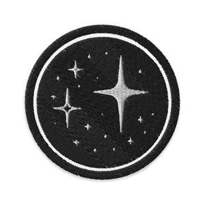 Puede incluir: Parche bordado circular con fondo negro y borde blanco. El diseño presenta estrellas blancas y estrellas más pequeñas, evocando un tema celestial. Ideal para ropa o accesorios.