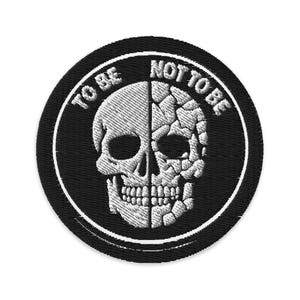 May include: A black, round embroidered patch featuring a skull design split vertically. One half of the skull is intact, the other is fragmented. The words "TO BE" and "NOT TO BE" are embroidered around the skull in white.