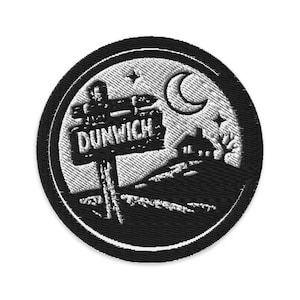 Puede incluir: Parche bordado negro que representa una escena nocturna con un letrero que dice "DUNWICH". El diseño incluye una luna creciente, estrellas y la silueta de un edificio. El parche tiene un borde negro.