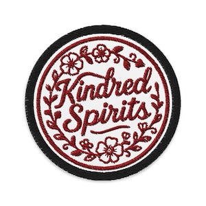 Puede incluir: Parche bordado circular con la frase "Kindred Spirits" en escritura burdeos, rodeado por una corona floral. El parche tiene un centro blanco, un borde burdeos y un borde exterior negro.
