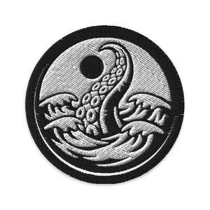 May include: Embroidered patch featuring a white kraken tentacle emerging from stylized waves within a white circle. The circle is set against a black background, creating a striking contrast. The design is detailed and textured.